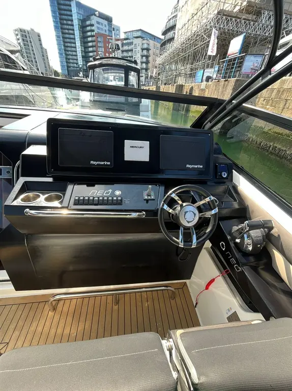 Cockpit view of a modern boat highlighting Raymarine displays, steering wheel, and surrounding urban marina scenery.